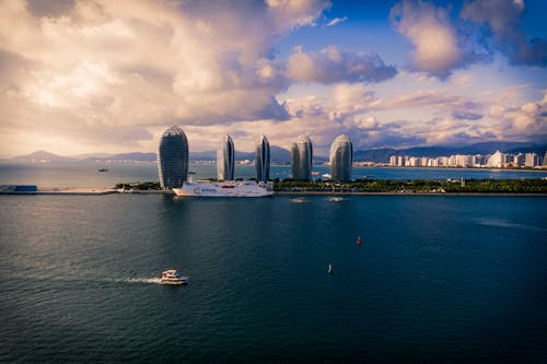 Modern cruise ships and boats floating on calm sea against cloudy sky near futuristic skyscrapers located on Phoenix Island in China