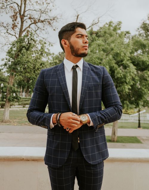 Free Serious ethnic businessman with bracelets and wristwatch in formal suit and tie standing on street with trees behind Stock Photo