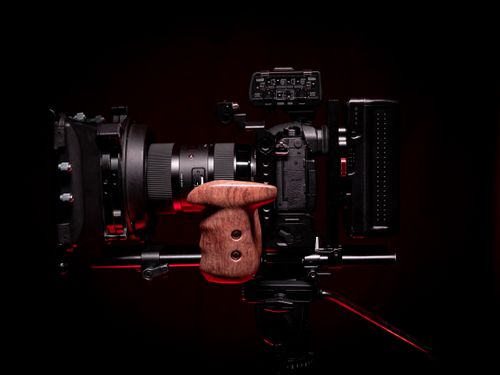 Free Close-up of a professional video camera setup with a wooden grip against a dark background. Stock Photo