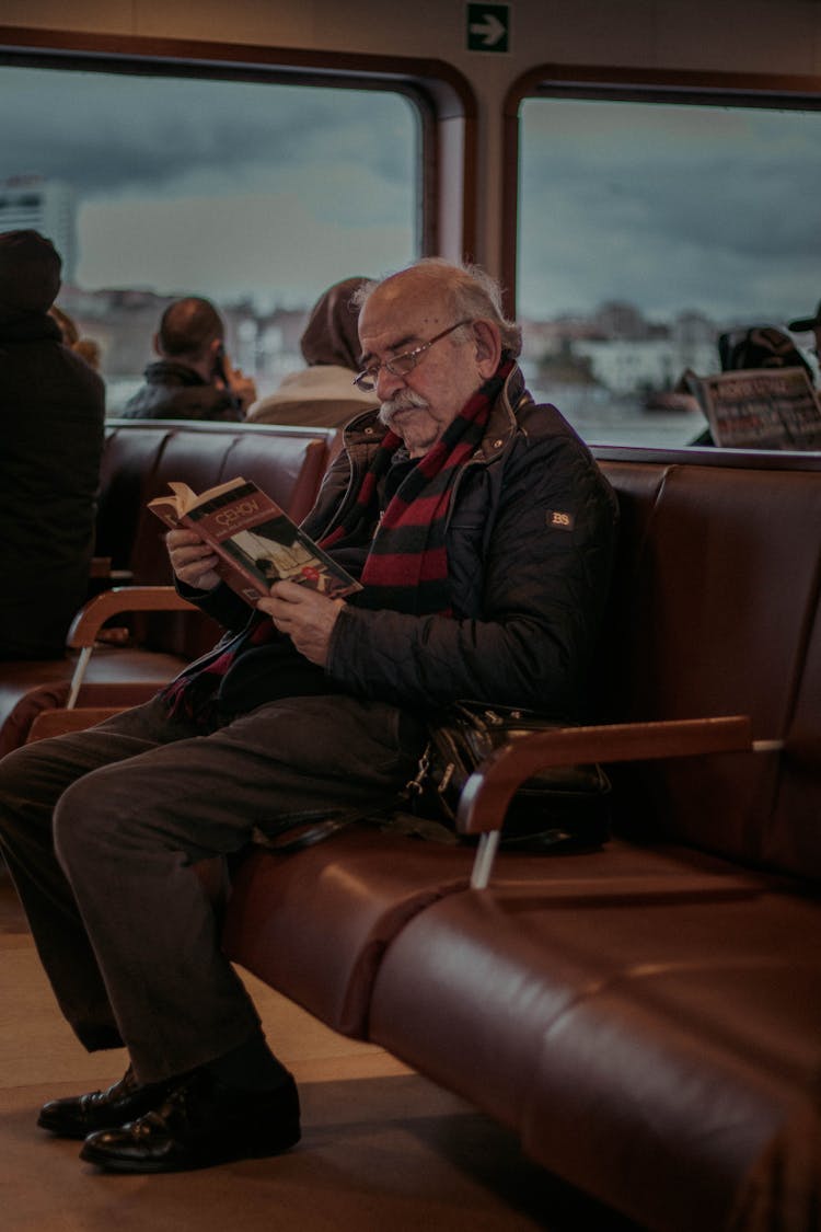 Senior Man Reading Book In Bus Terminal