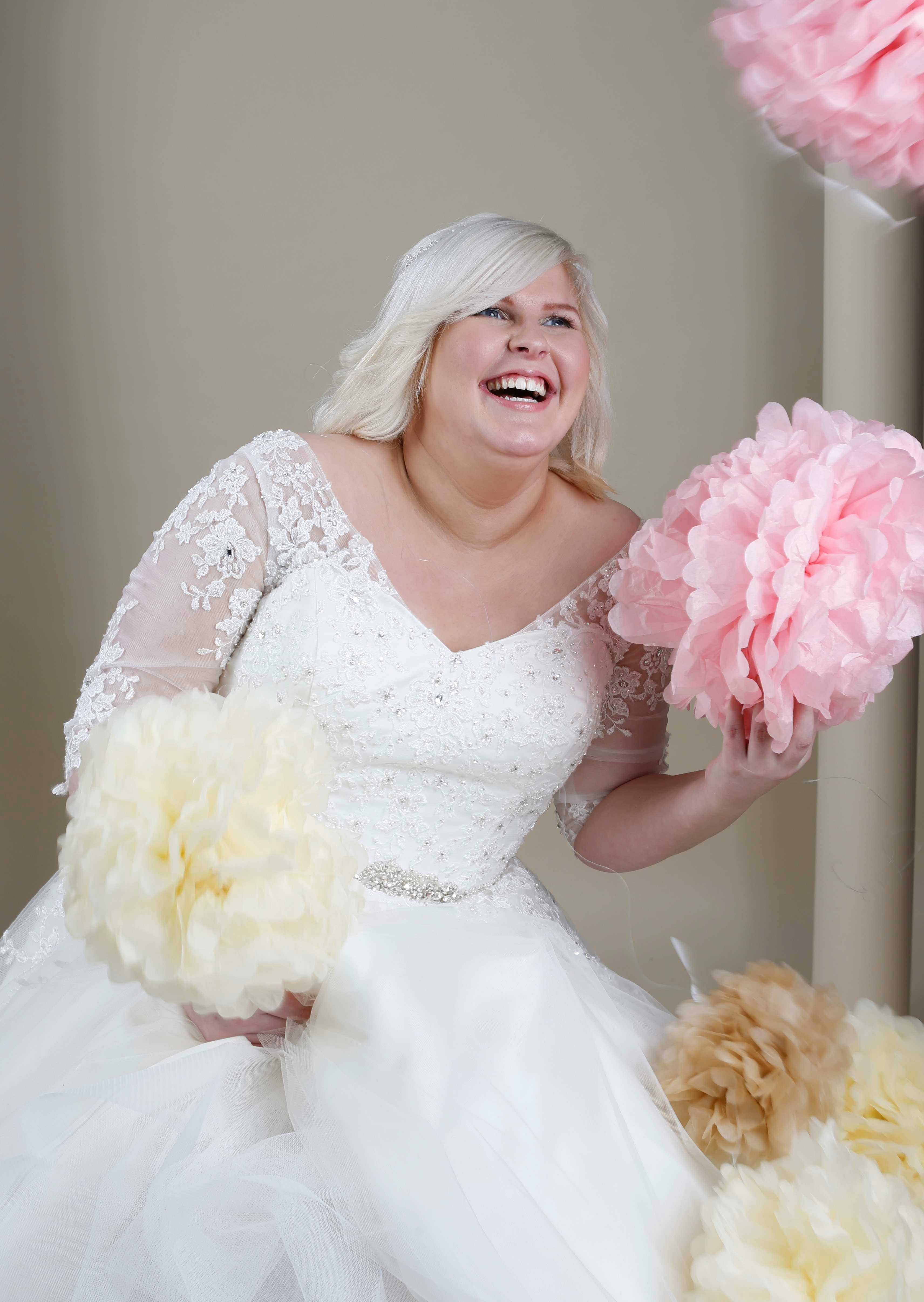 Happy bride in a wedding dress holding colorful pom-poms indoors.