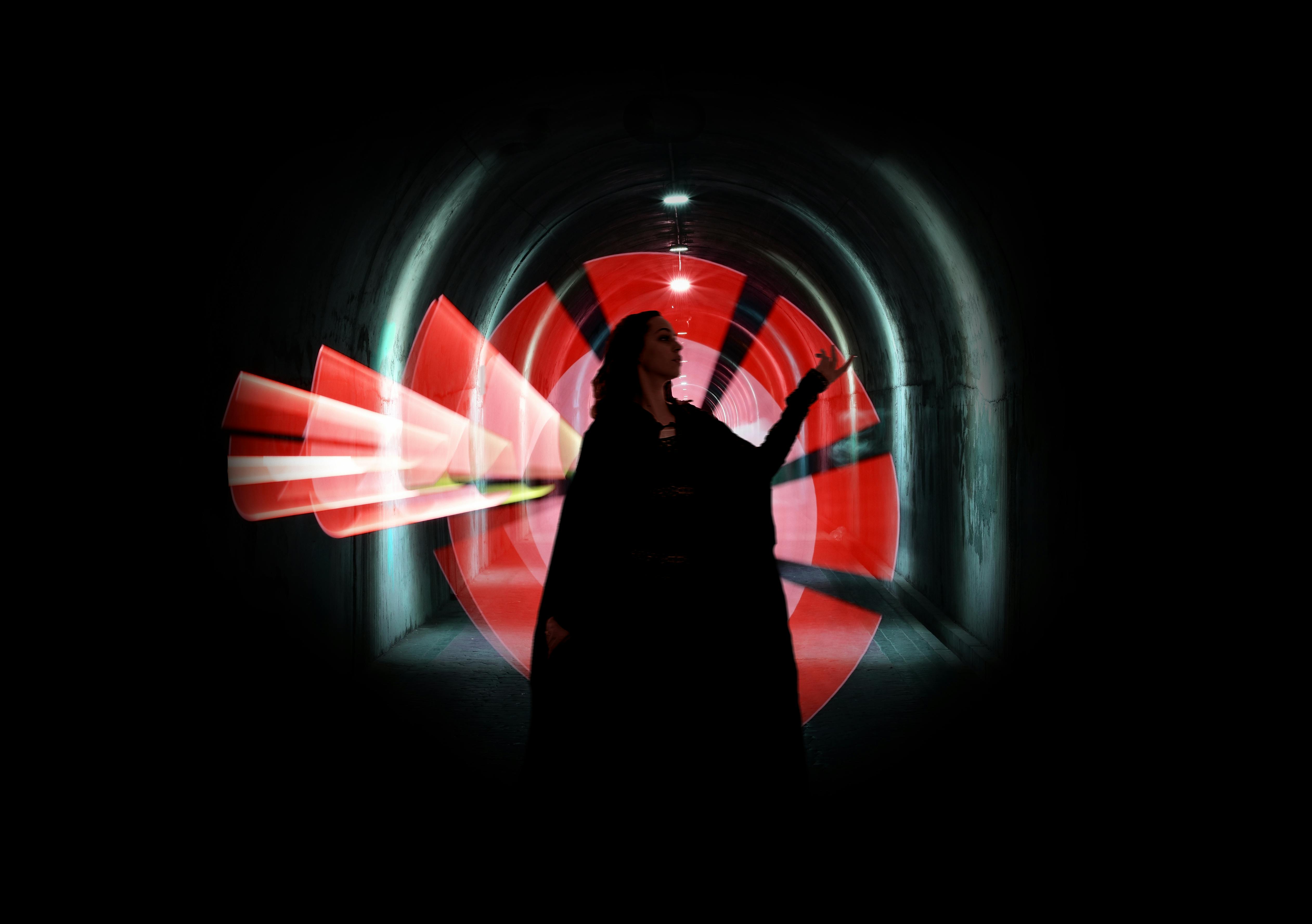 A silhouetted figure stands in a tunnel with dynamic red and neon light painting effects.