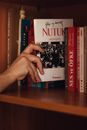 Anonymous person putting red paper book in hardcover on shelf in wooden closet in bright room