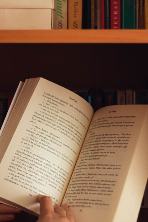Free Unrecognizable person reading interesting novel while standing near wooden bookcase in cozy apartment Stock Photo