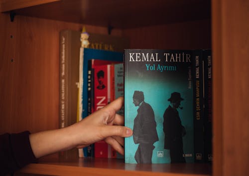 Crop woman showing book on bookshelf at home