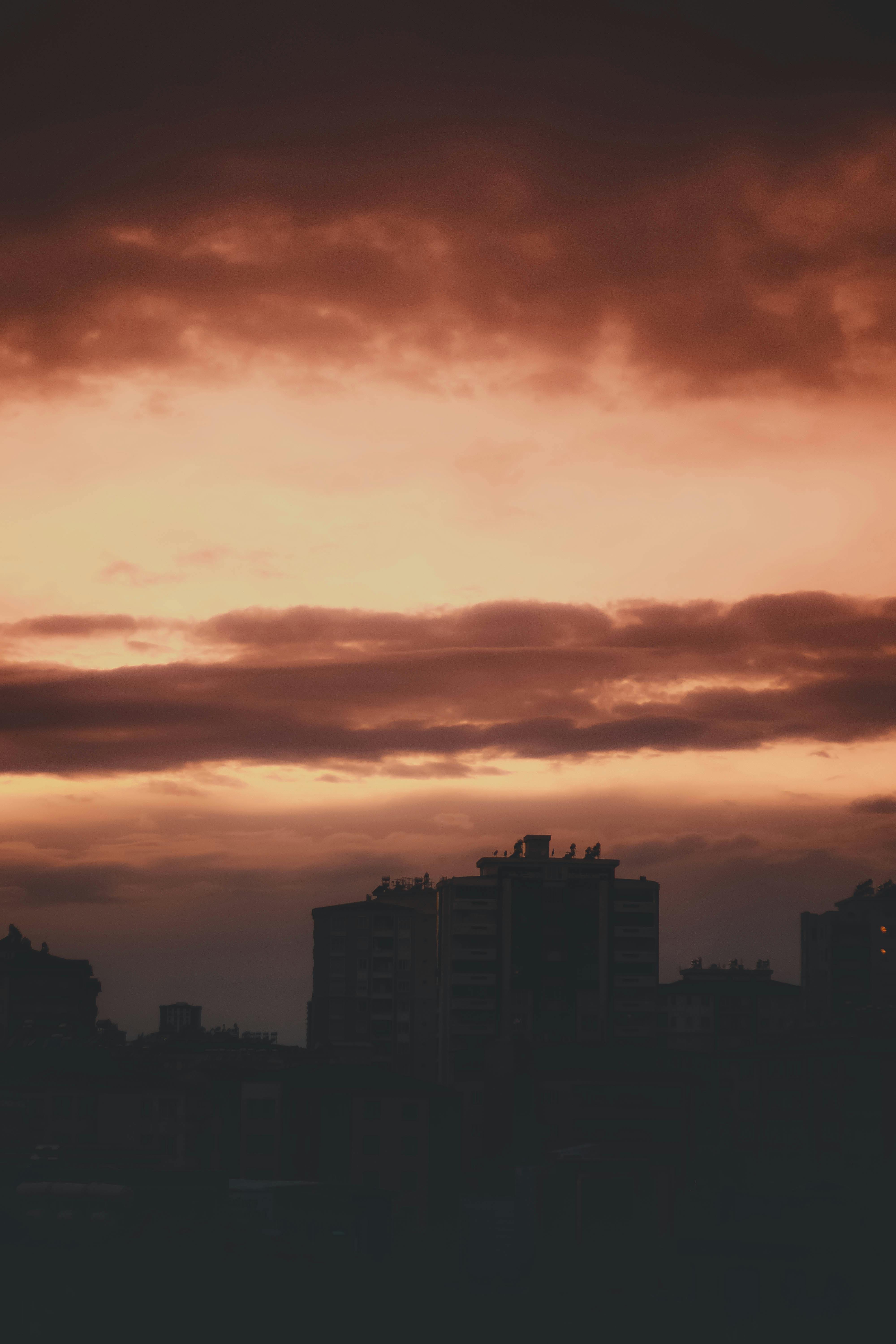 brown sky illuminating silhouettes of modern city buildings at sunset