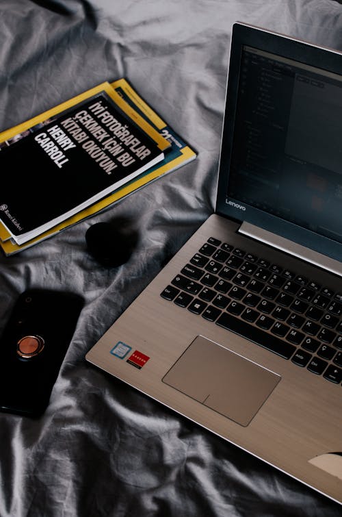 Modern laptop and books near smartphone on crumpled bed