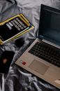 Modern laptop and books near smartphone on crumpled bed