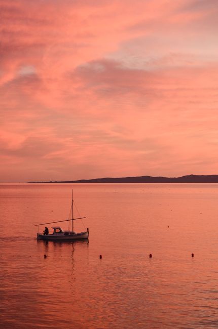 A fishing boat floats on the calm Adriatic Sea at sunset near Croatia, capturing a tranquil moment.