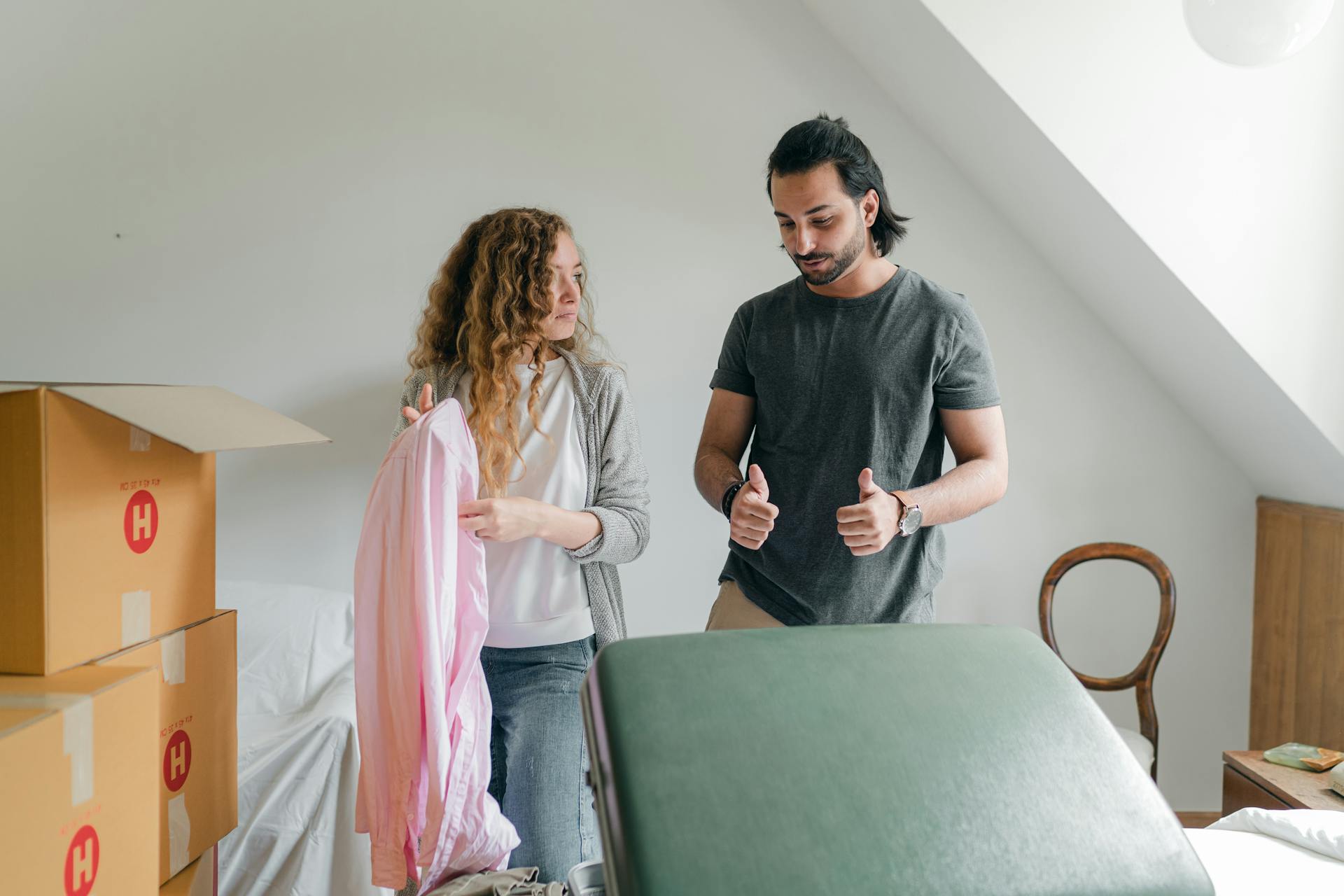 Positive young couple in casual clothes packing belongings into carton boxes and discussing new home while moving in together