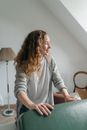 Positive lady wearing casual clothes closing packed suitcase and smiling while standing in sunny bedroom and anticipating journey abroad