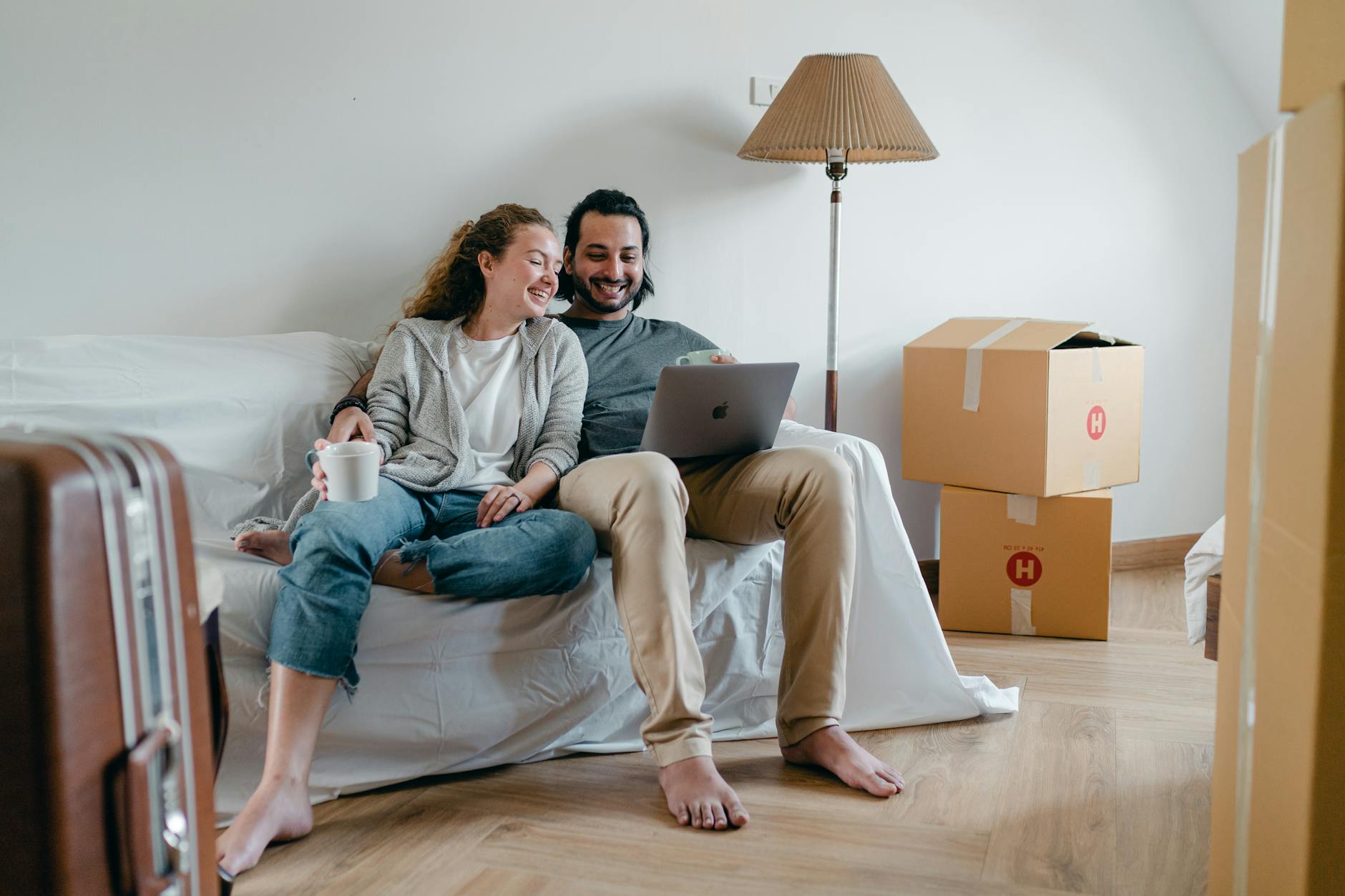 Cheerful couple watching video on laptop together while sitting on couch in living room when moving house