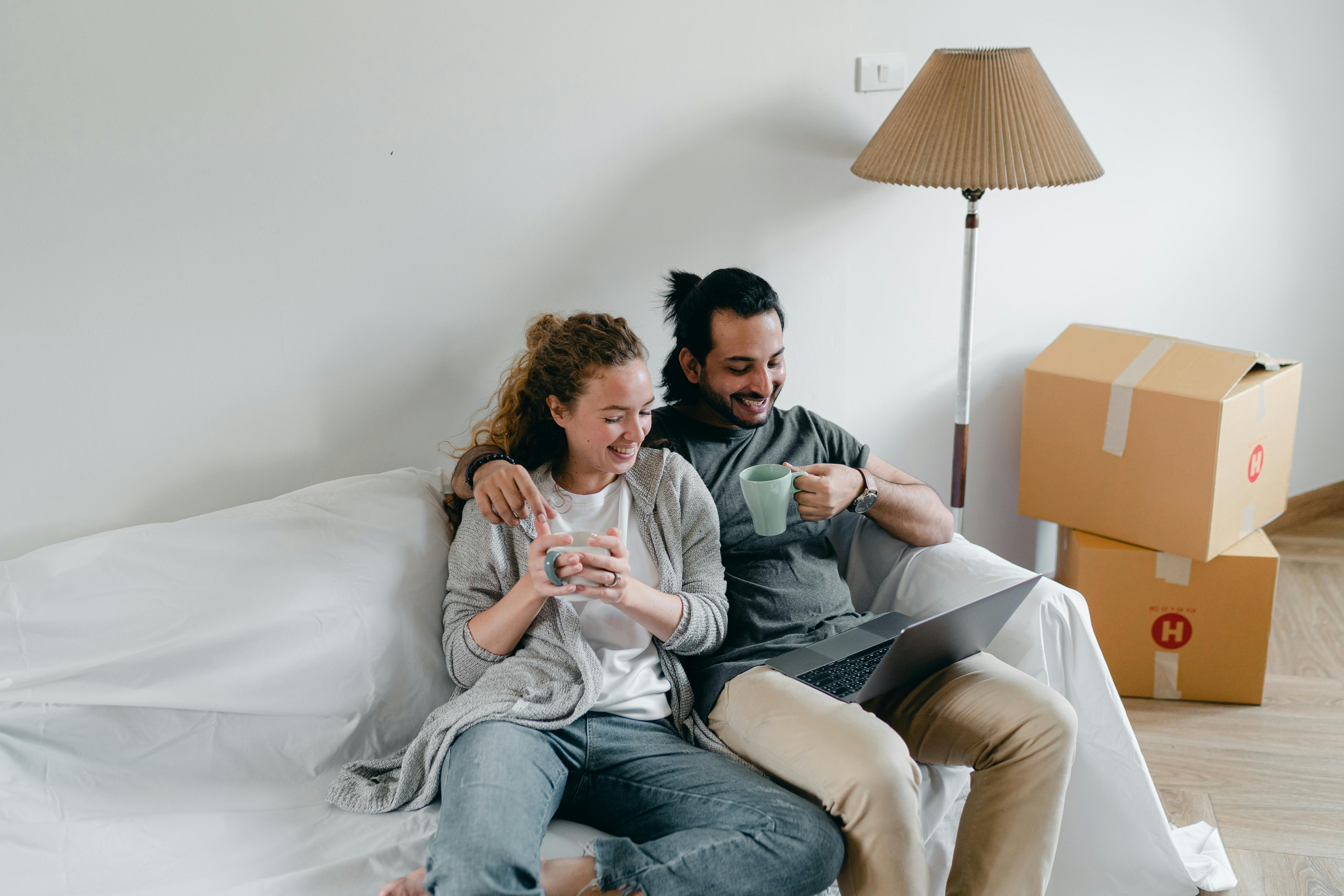 multiethnic couple embracing on couch while watching laptop at home