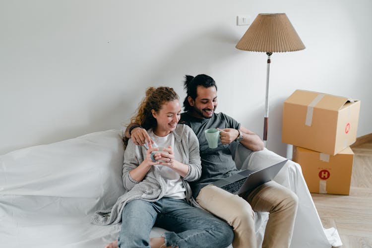 Multiethnic Couple Embracing On Couch While Watching Laptop At Home