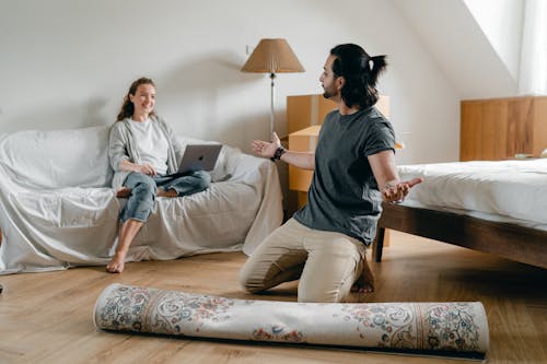 Happy woman with laptop looking at ethnic man with carpet