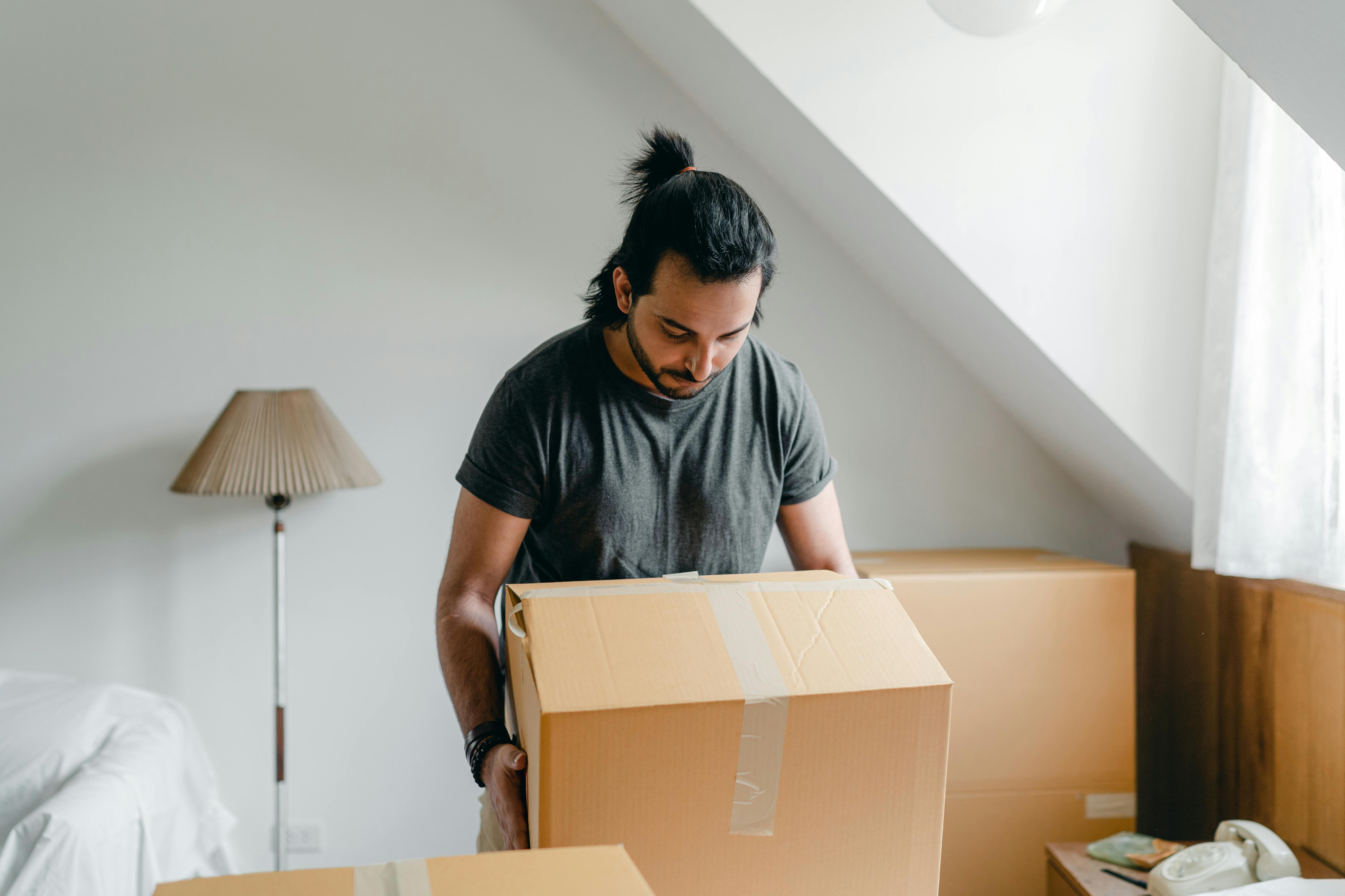 ethnic guy picking up cardboard box in house