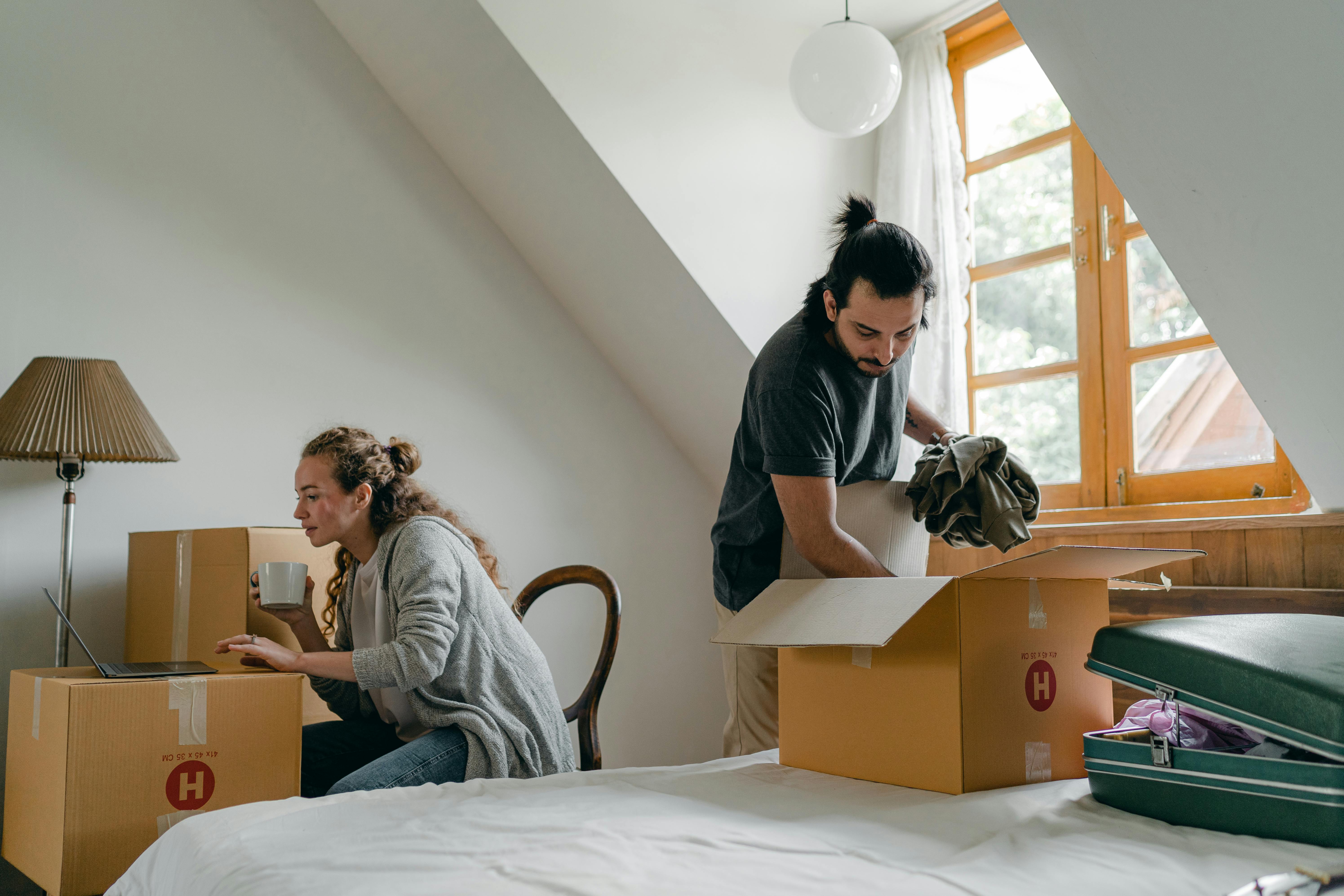 ethnic boyfriend unpacking box while woman using laptop at home