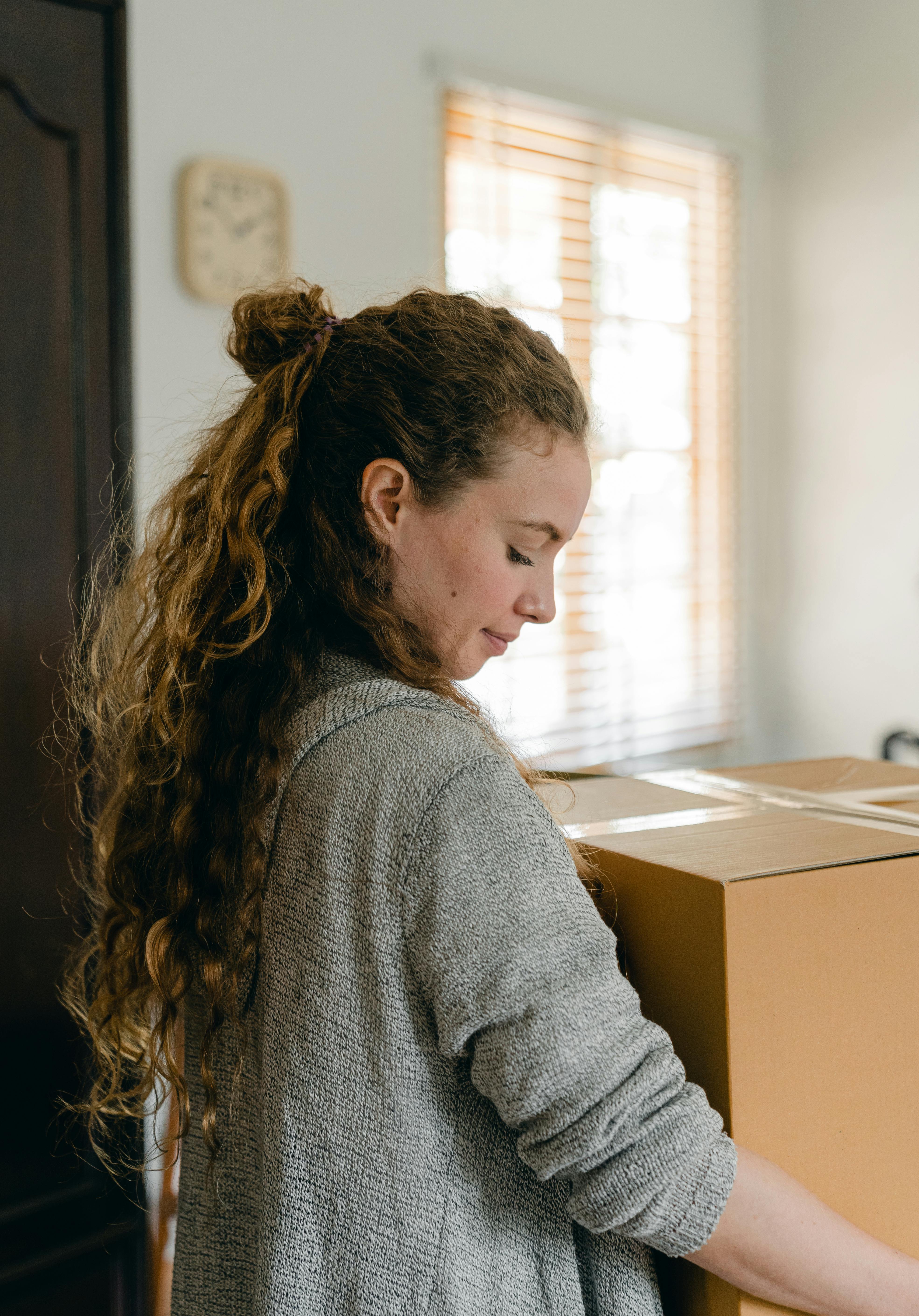 adult pensive woman holding big cardboard box in apartment