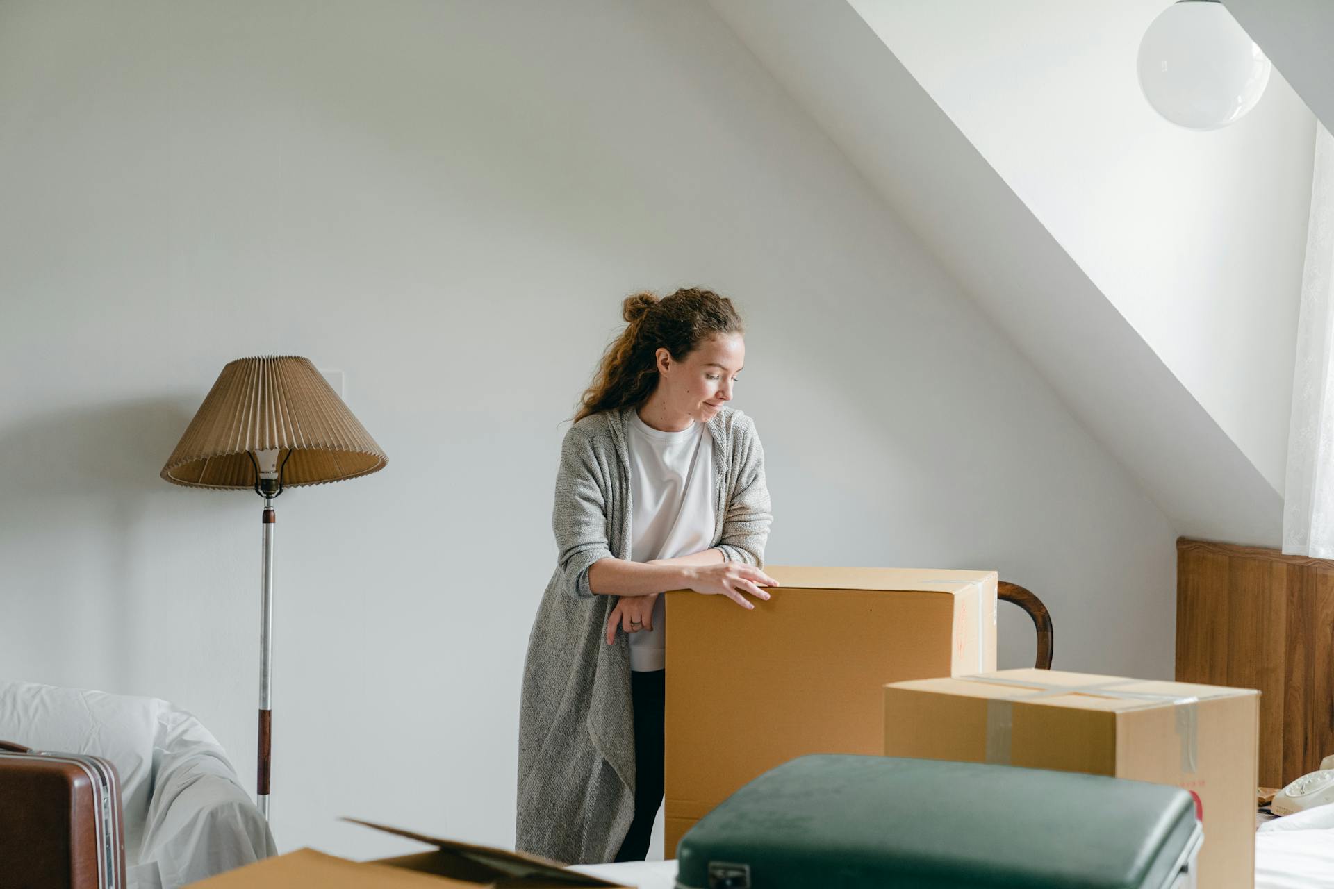 Woman in a calm setting, pondering on relocation with moving boxes in an attic room.