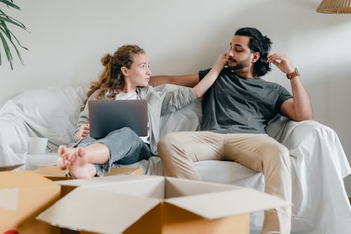 Girlfriend with laptop touching ethnic face of man on sofa