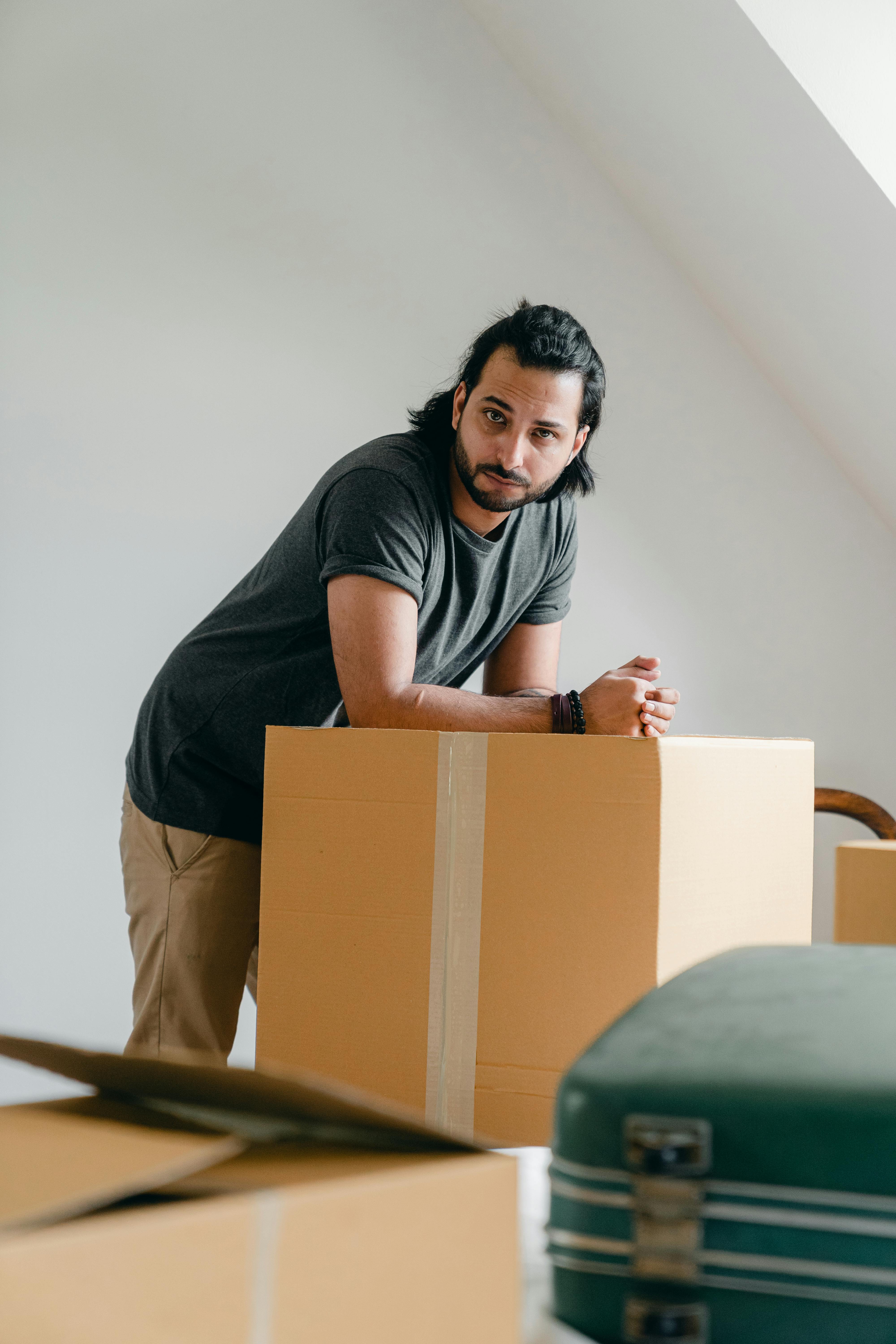 pensive ethnic man leaned on cardboard box at home