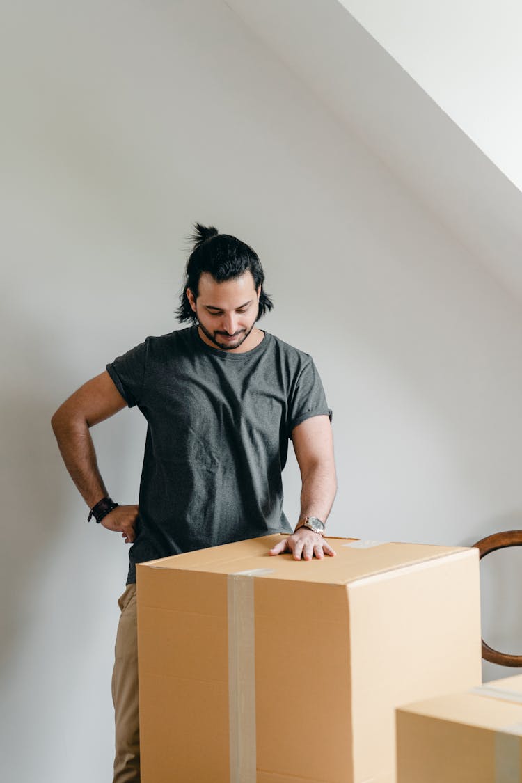 Smiling Ethnic Man In Wristwatch Touching Cardboard Box In House