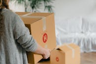 Crop anonymous woman holding big box near sofa in apartment