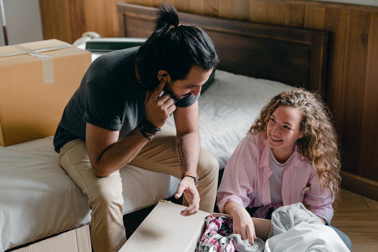 Happy Woman With Man Unpacking Box Of Clothes