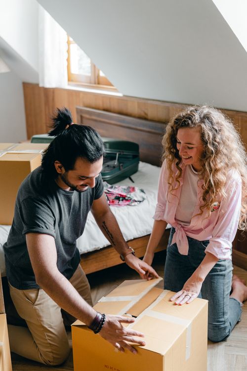 Free Smiling female and male in casual outfit sitting on floor in bedroom while packing carton box and moving to new flat Stock Photo