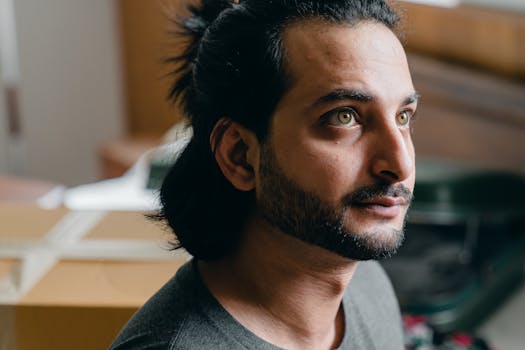 A young man with a thoughtful expression in a cozy, new apartment environment.