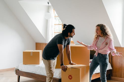 Serious multiethnic couple in trendy casual clothes discussing about relocation while woman gesticulating during unpacking things in spacious modern apartment