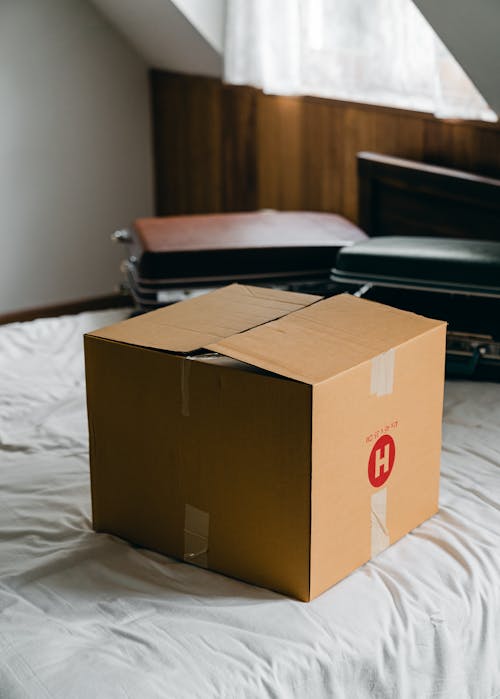 High angle of suitcases stacked behind carton box on bed in contemporary bedroom