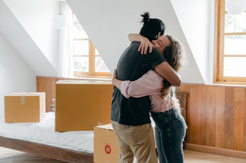 Free Side view of young multiethnic couple embracing each other while finishing relocation and standing near carton boxes in light spacious bedroom Stock Photo