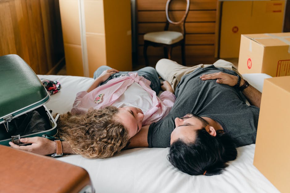 From above of diverse young couple in casual outfit hugging on bed between boxes and suitcases while resting together in modern bedroom during relocate