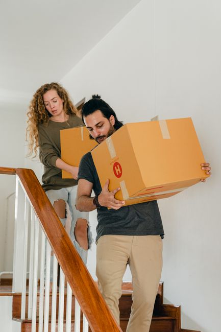 A couple carrying a moving box down the stairs of a family home.