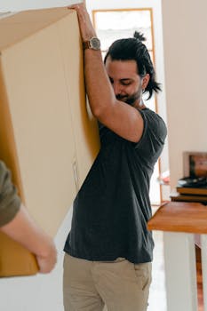 Unrecognizable couple in casual clothes helping each other moving personal items in carton box to new apartment