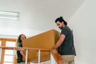 From below of couple in casual clothes carrying big carton box together while moving packed personal items into new apartment