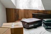 From above of brown and green vintage suitcases and packed carton boxes placed on bed with sheet in light room with sloping roof