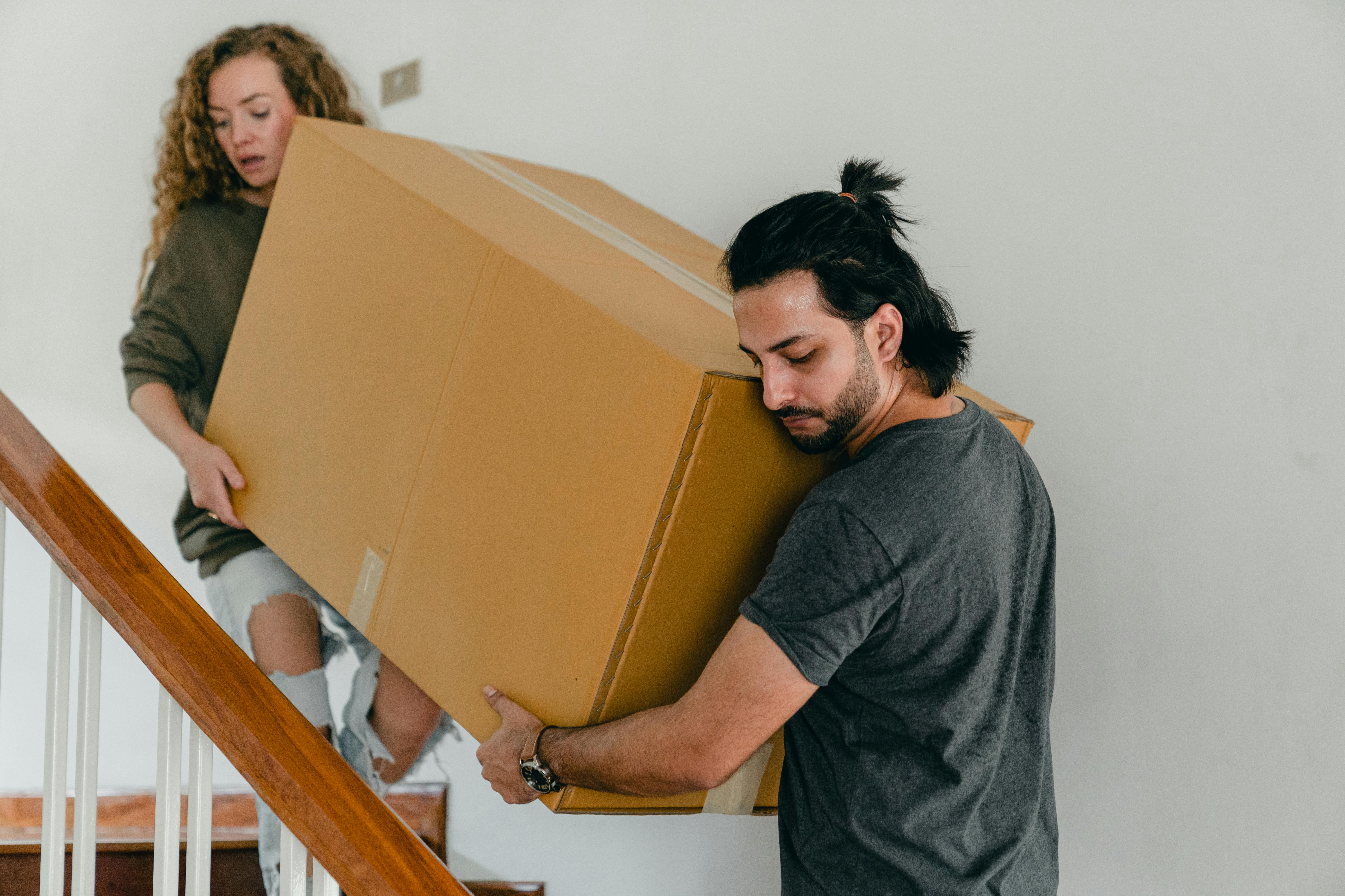 concentrated couple carrying big carton box down stairs