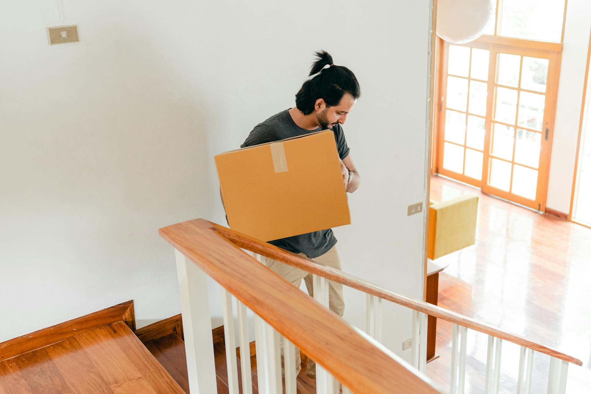 From above of full length male in casual clothes carrying carton box down stairs while moving personal items to new house