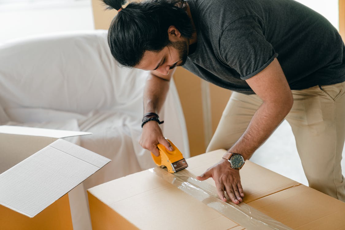 Adult man packing cardboard box with scotch tape dispenser