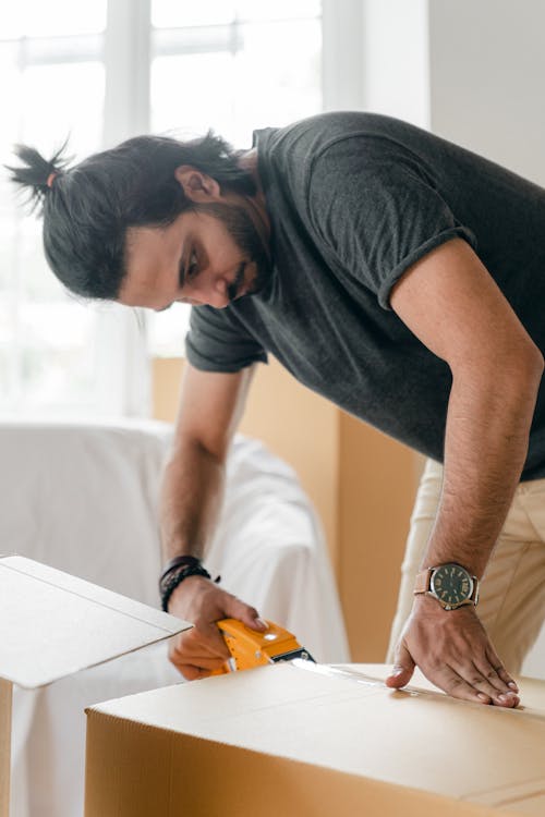 Focused young man taping cardboard box for storage