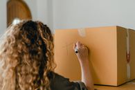 Back view of faceless young lady with curly hair preparing cardboard boxes for moving