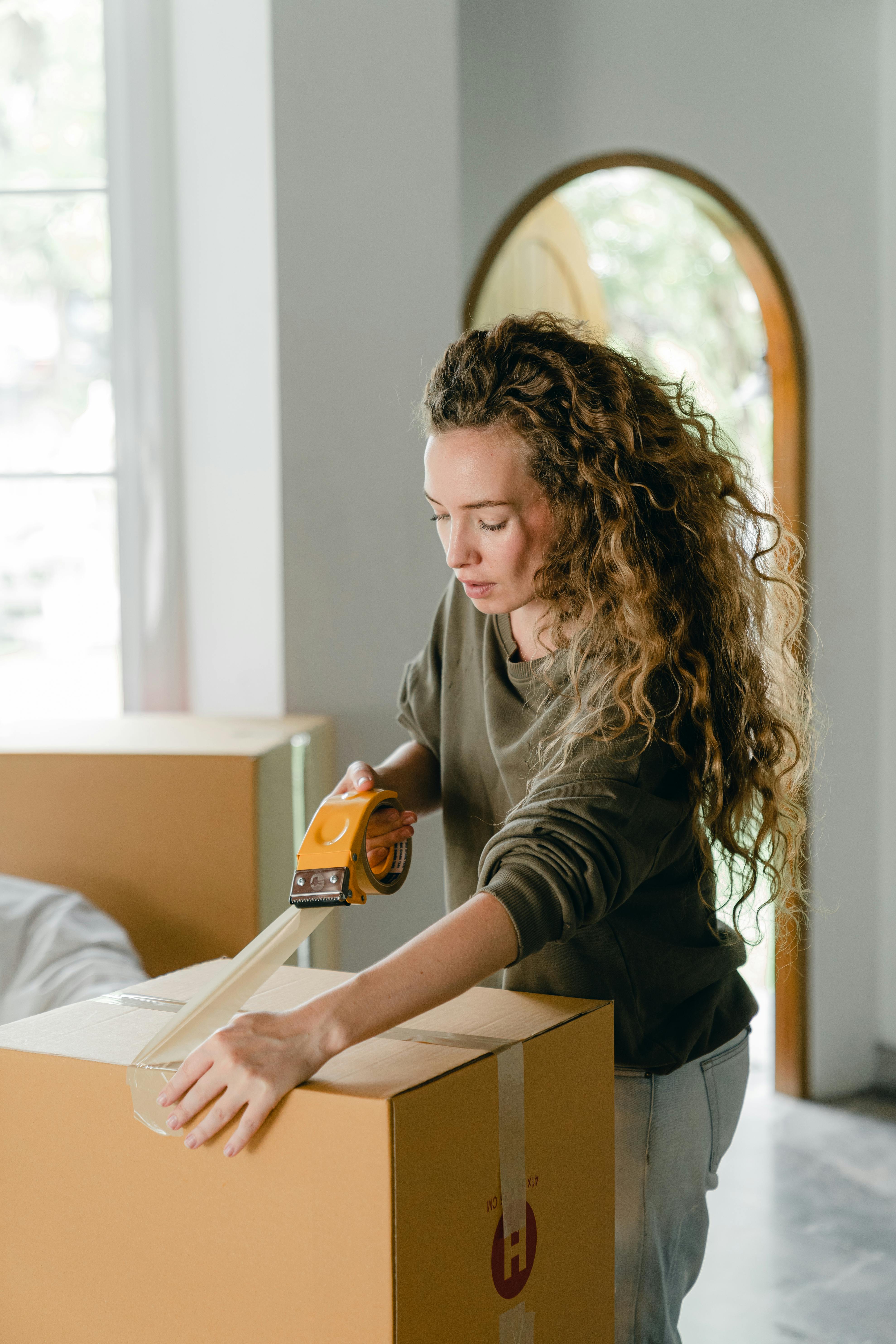 concentrated young lady sealing cardboard boxes at home