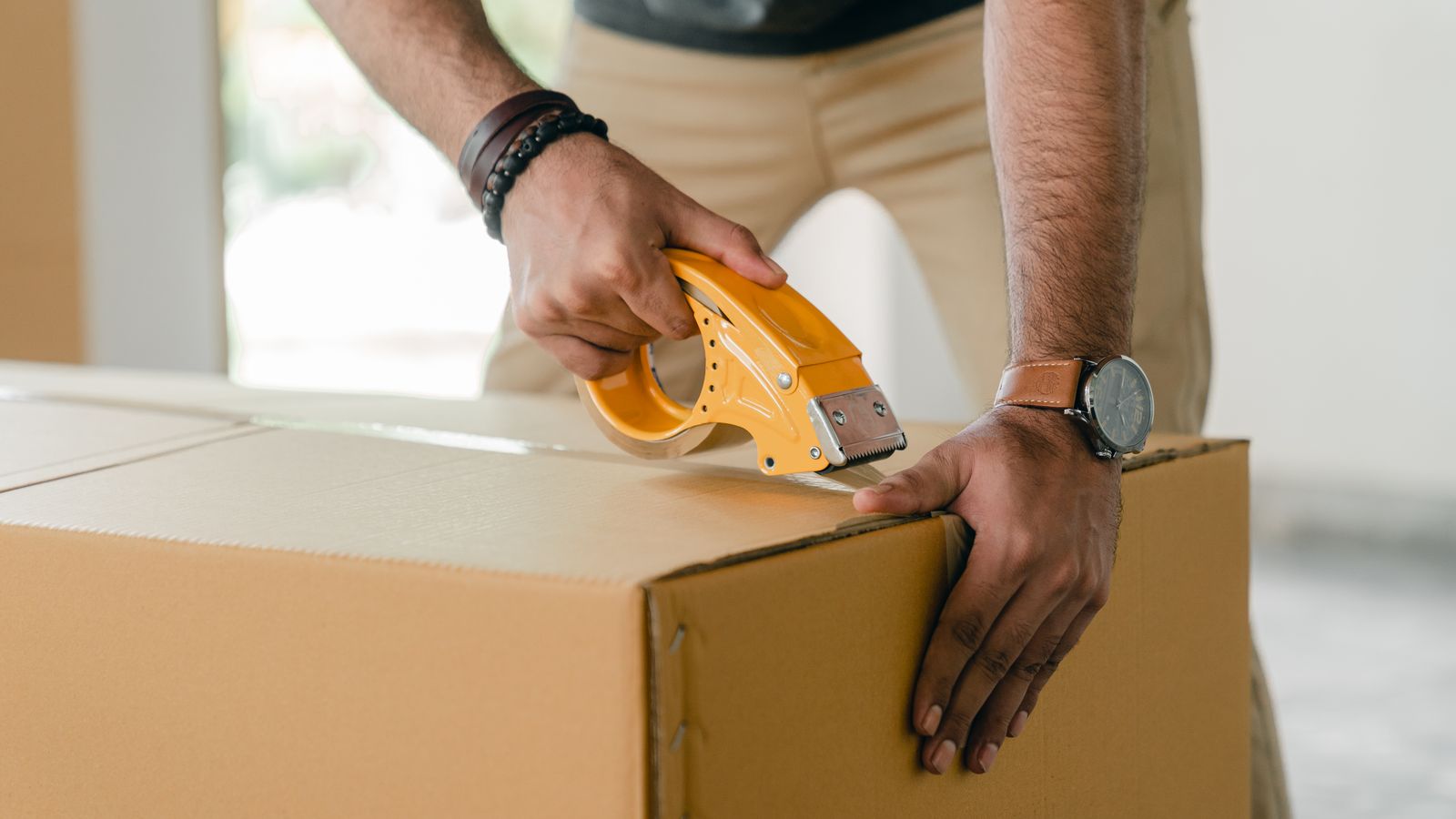 Person verschliesst beim Packen einen Umzugskarton mit Klebeband.