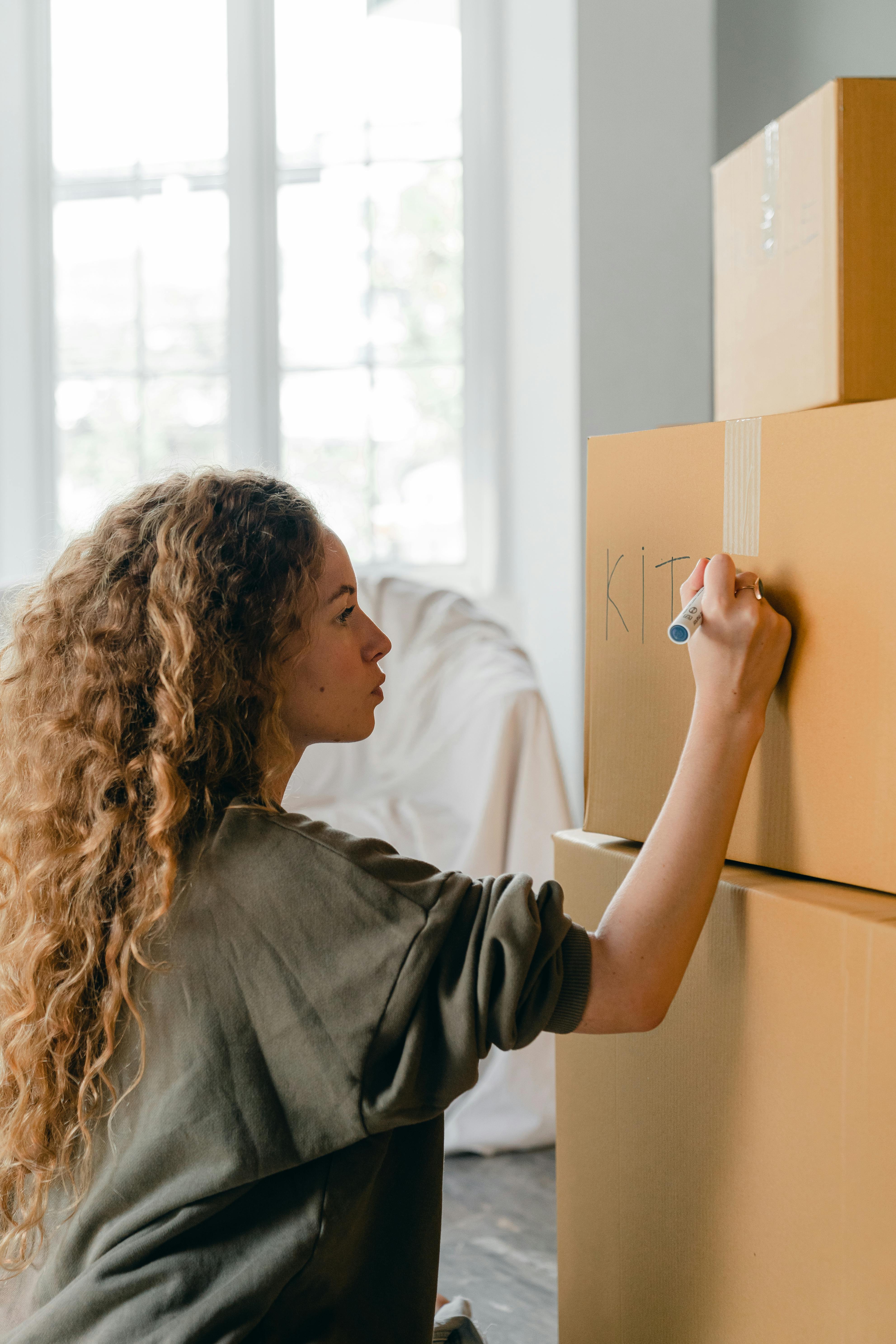 focused young female writing on cardboard boxes and preparing for relocation