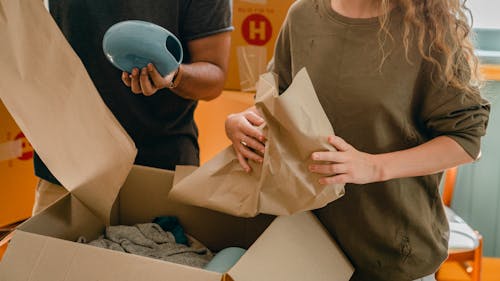 Crop faceless young woman and man unpacking belongings after moving in new house