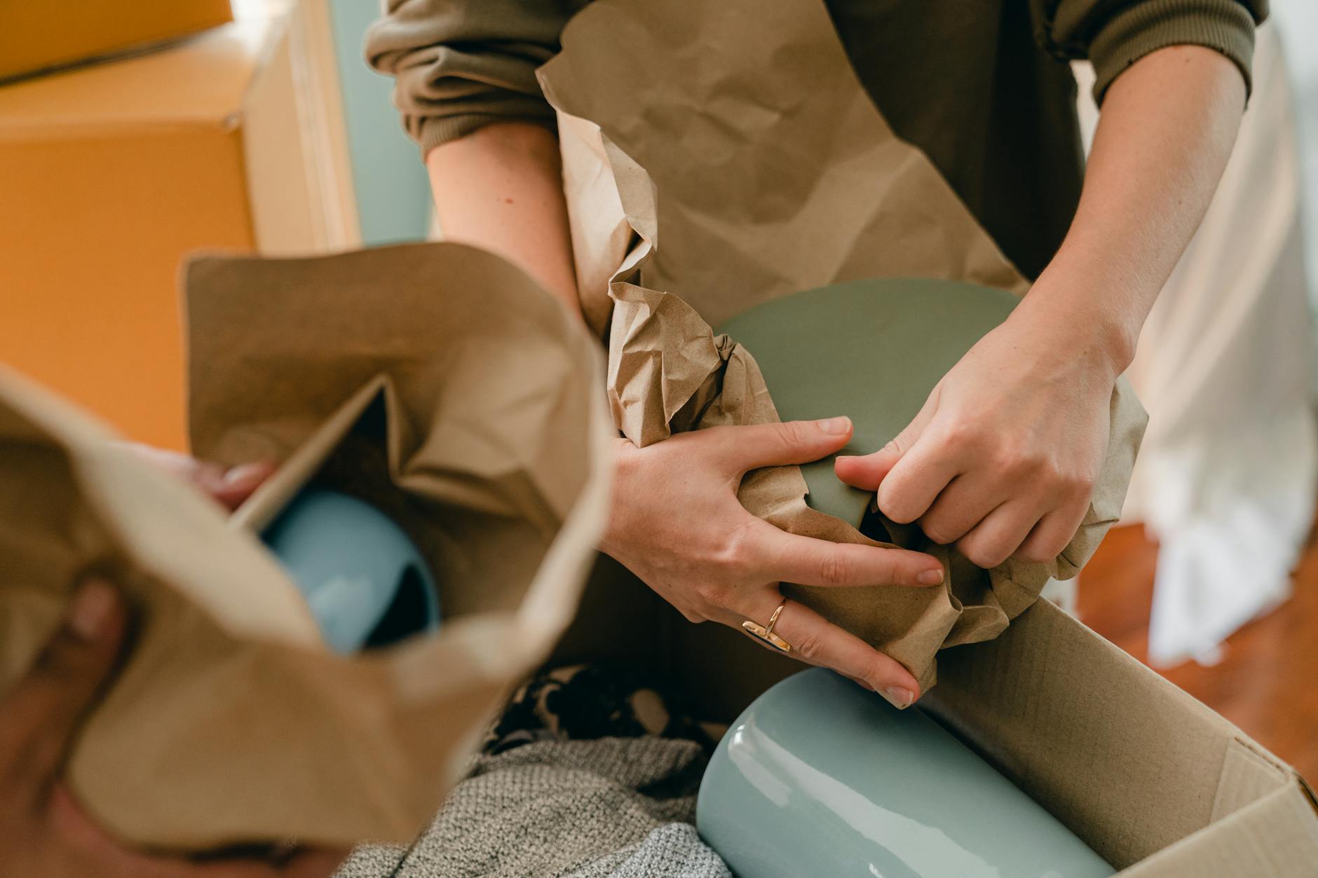 Crop unrecognizable person packing ceramic tableware in parchment