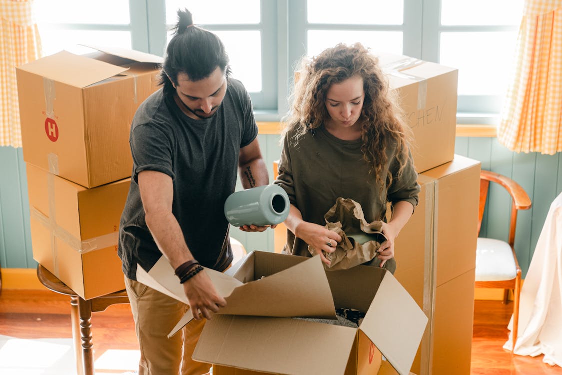 Free Multiethnic couple packing belongings in parchment near pile of boxes Stock Photo