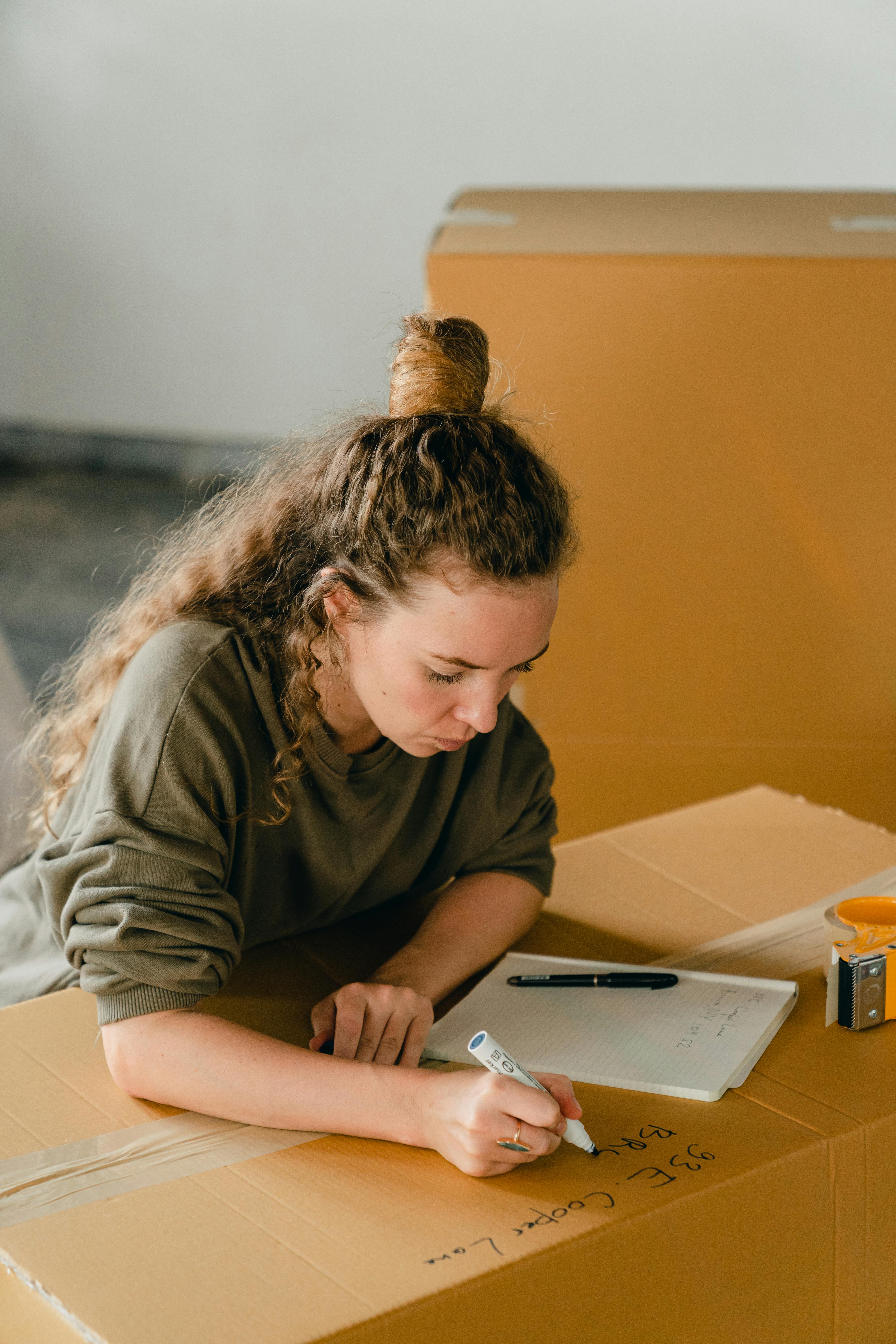 adult woman signing cardboard box with marker in flat